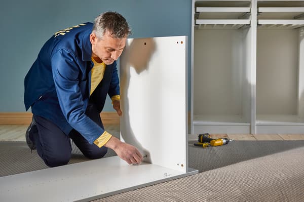 En mann i IKEA-uniform monterer et garderobeskap. 