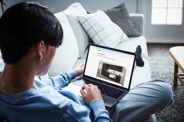 En mann sitter i en hvit sofa og planlegger kjøkken på en laptop.
