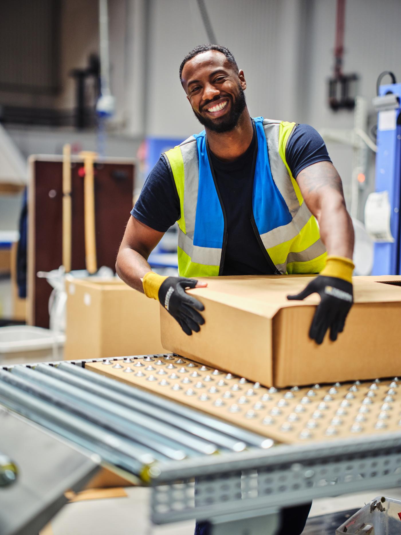 En medarbetare håller om ett paket som ligger på ett band. Personen tittar upp och ler mot kameran.