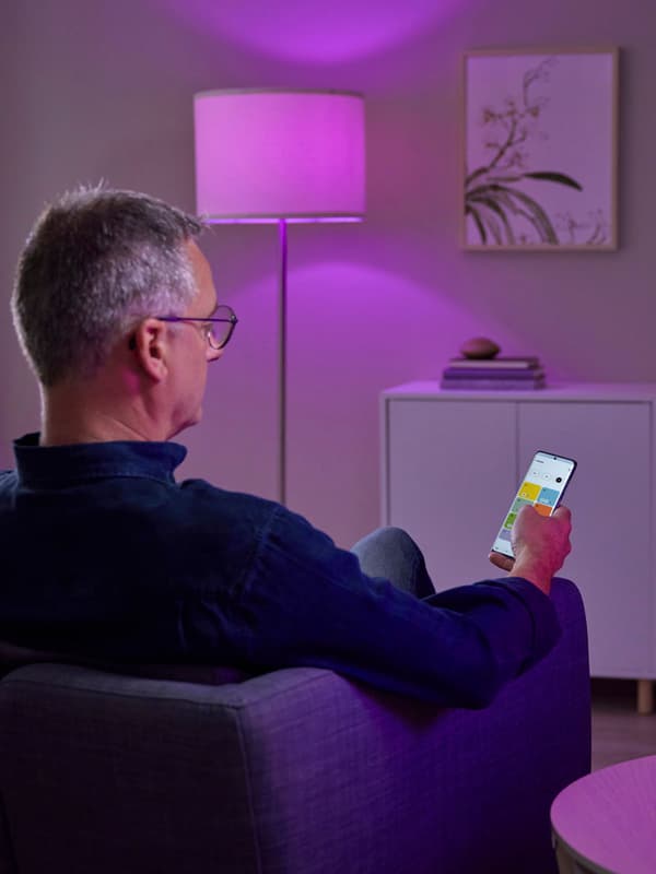 En mobil enhet som visar appen IKEA Home smart, med en TRÅDFRI genvägsknapp och hubben DIRIGERA intill.