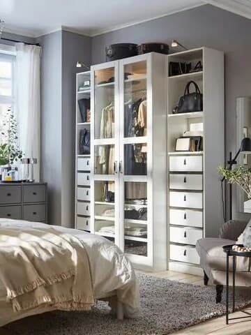 En öppen garderobslösning framför en IKEA säng. I garderoben syns kläder och handväskor.