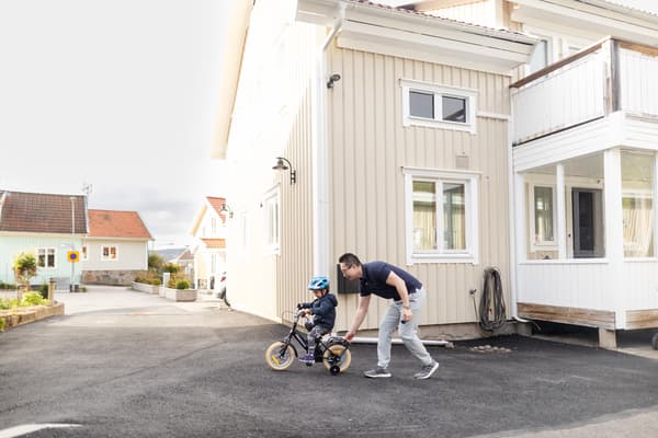 En pappa håller i en cykel med stödhjul som ett barn cyklar på. 