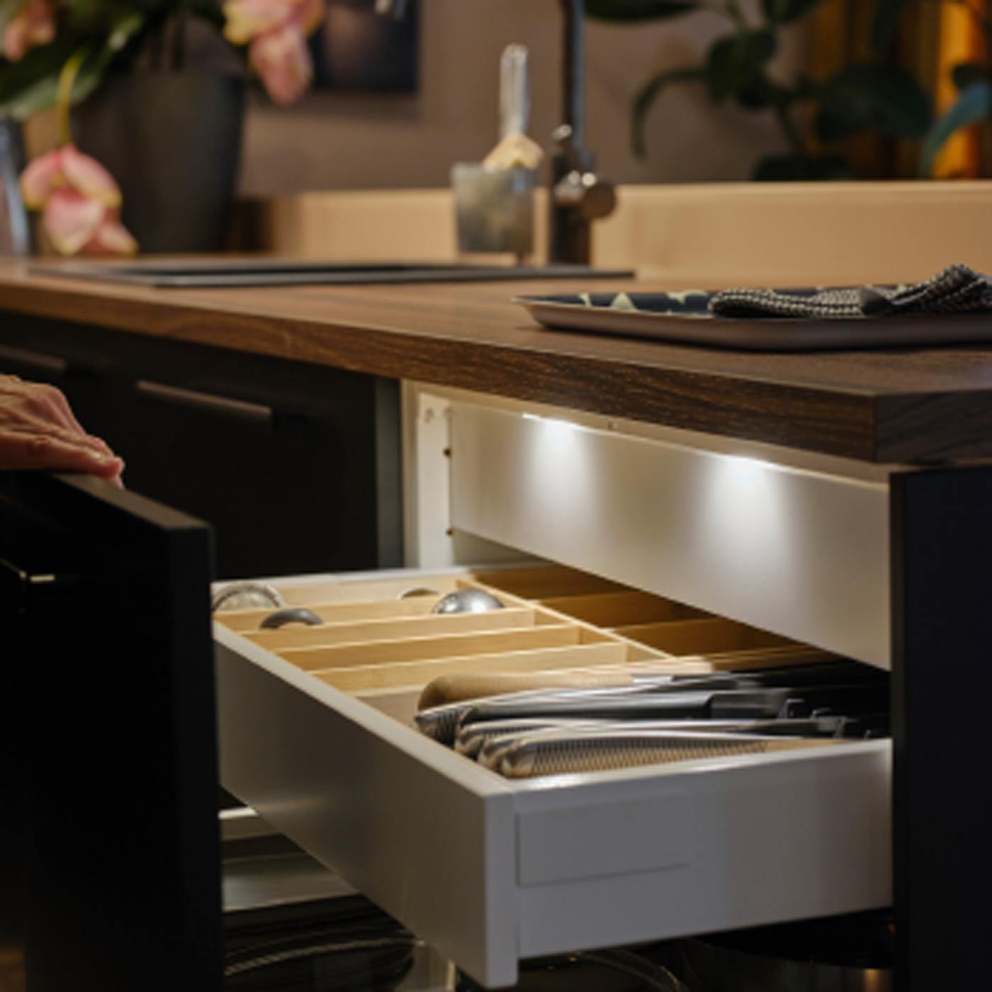 En person åbner en køkkenskuffe med en mat antracitgrå front, og der ses MITTLED LED-belysning i køkkenskuffer med sensor indeni.