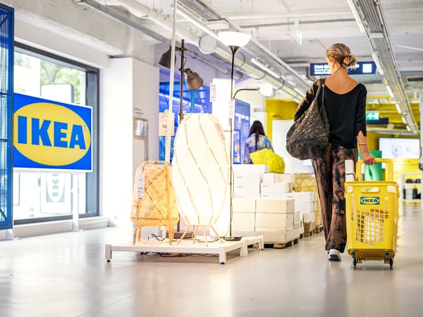 En person drar en gul kundkorg efter sig. Personen går genom ett IKEA-varuhus.