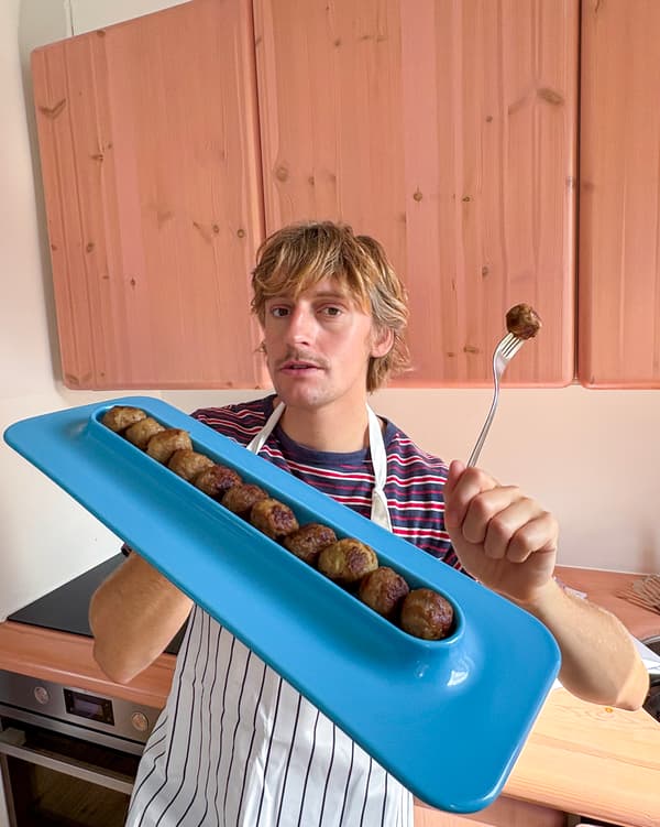 En person håller en avlång blå tallrik med köttbullar i ena handen. I andra handen håller personen en gaffel med en köttbulle på.