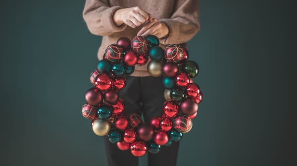 En person håller i en julkrans bestående av röda julgranskulor.