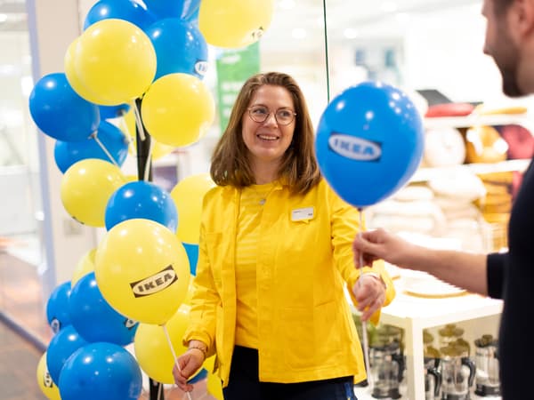 En person i gula kläder delar ut en blå ballong till en annan person.