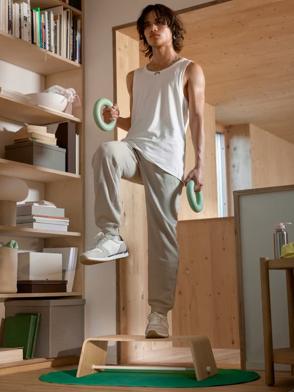 En person i träningskläder står med hantlar i händerna och tränar på en step-up-bräda.