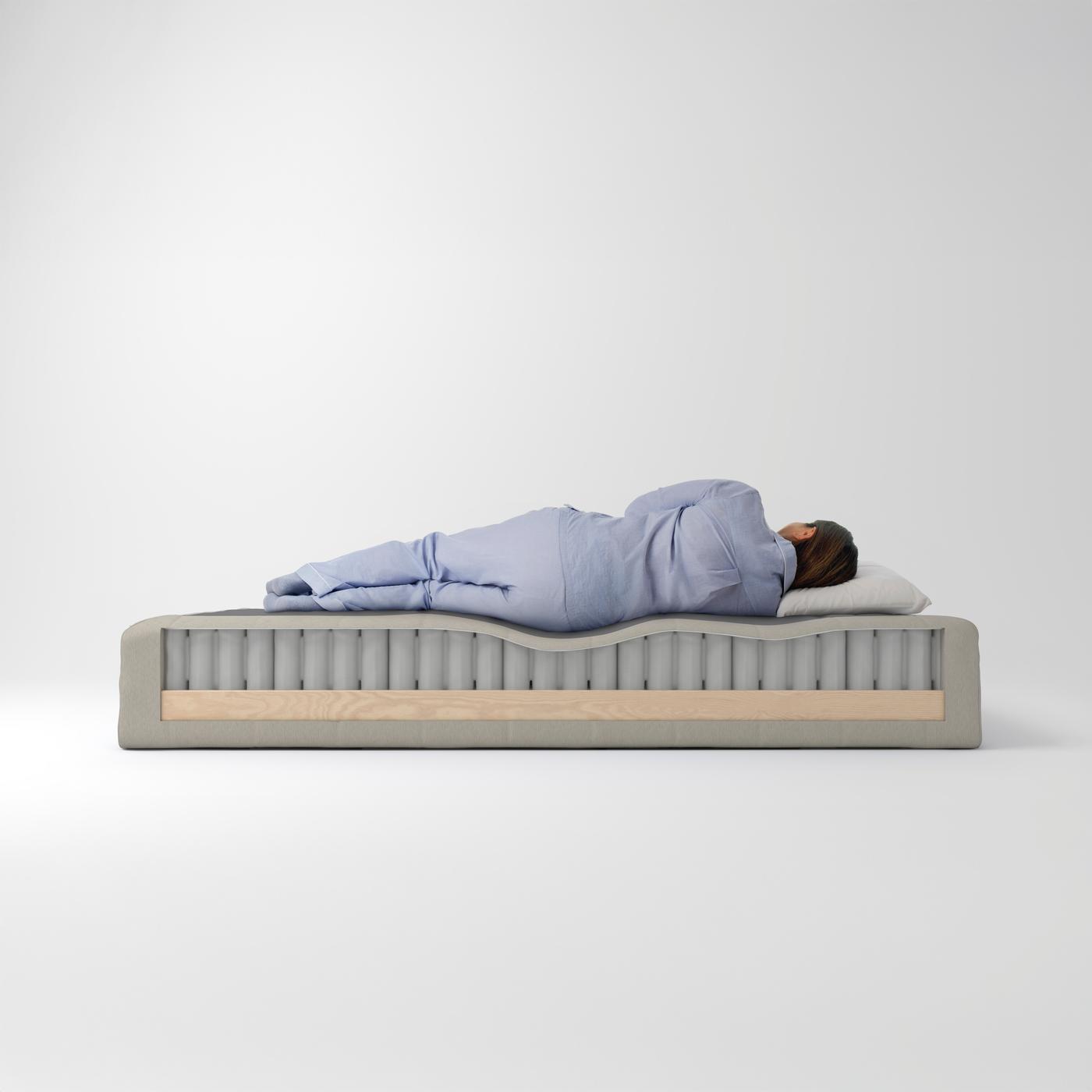 En person ligger och sover på en FEMTÅSEN pocketresårkärna som har fått en del av sin träbas borttagen på ena sidan.