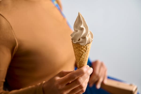 En person med mörkt beige tröja håller i en glasstrut. 
