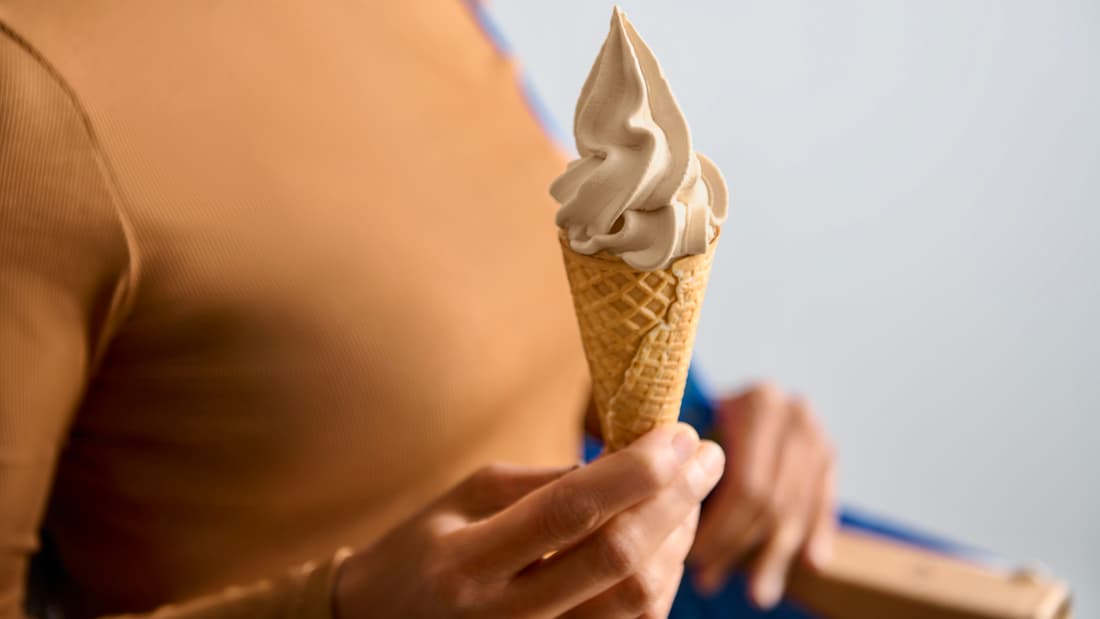 En person med mörkt beige tröja håller i en glasstrut. 