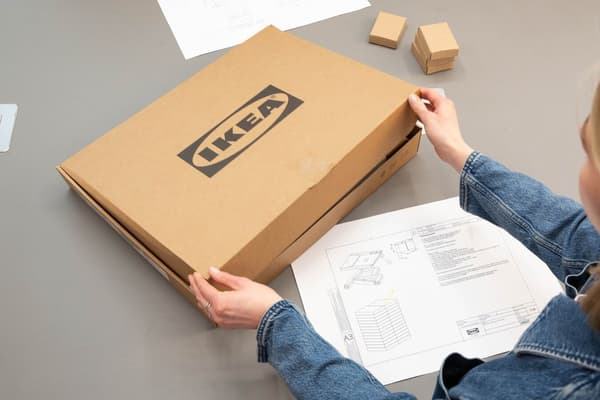 En person packar ner en öppnad IKEA‑produkt i en låda igen och returnerar den.