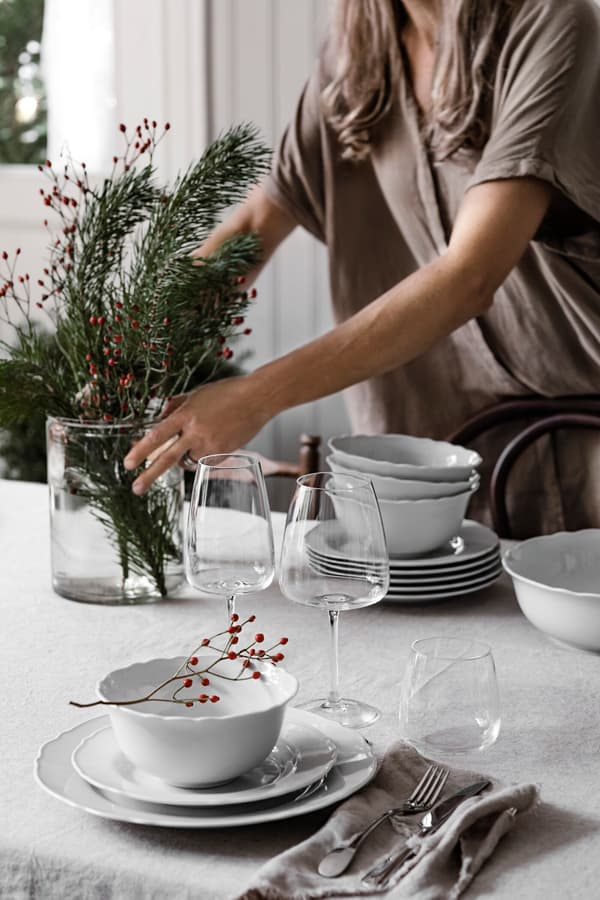 En person placerer en vase med grangrene på et rustikt julebord.
