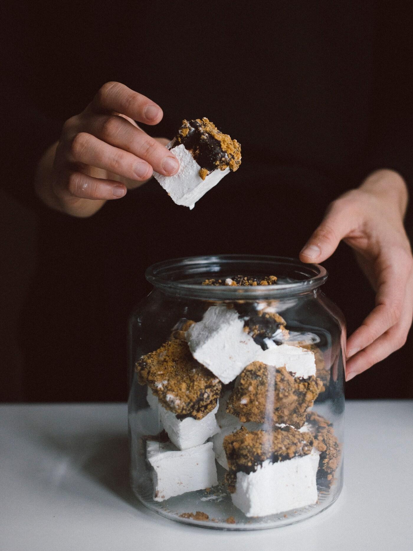 En person plockar upp en marshmallow ur en glasburk.