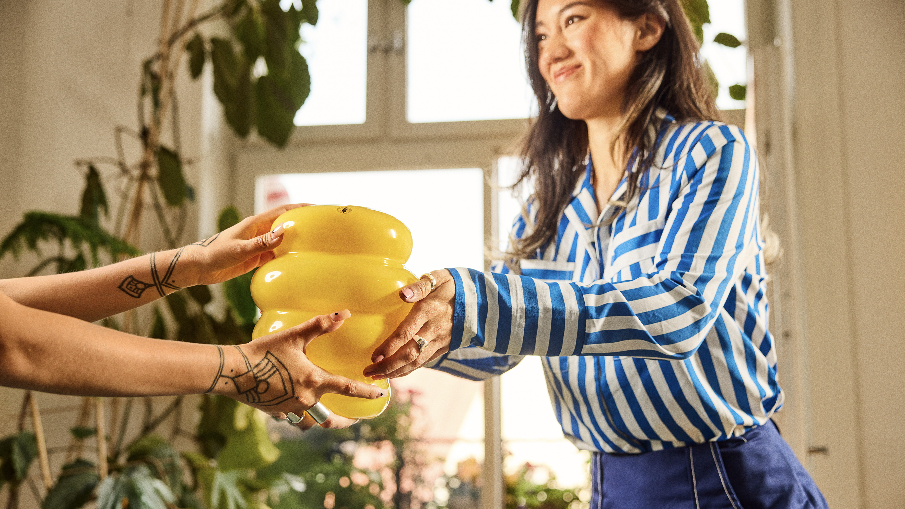 En person räcker över en gul vas till en annan person. 