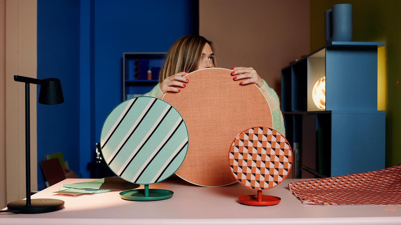 En person sitter bakom ett skrivbord. På skrivbordet står tre runda högtalare i olika storlekar och färger.