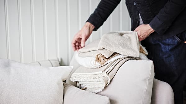 En person som viker en gråbeige GUNNEMOR pläd på armstödet på en ljusbeige SÖDERHAMN hörnsektion med en sits.