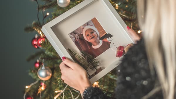 En person står framför en gran håller i en tavla med en bild på ett litet barn.