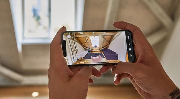 En person står i ett öppet rum och håller i en telefon samt använder IKEA-appen med IKEA Kreativ för att designa rummet i 3D-rumsplanerare.