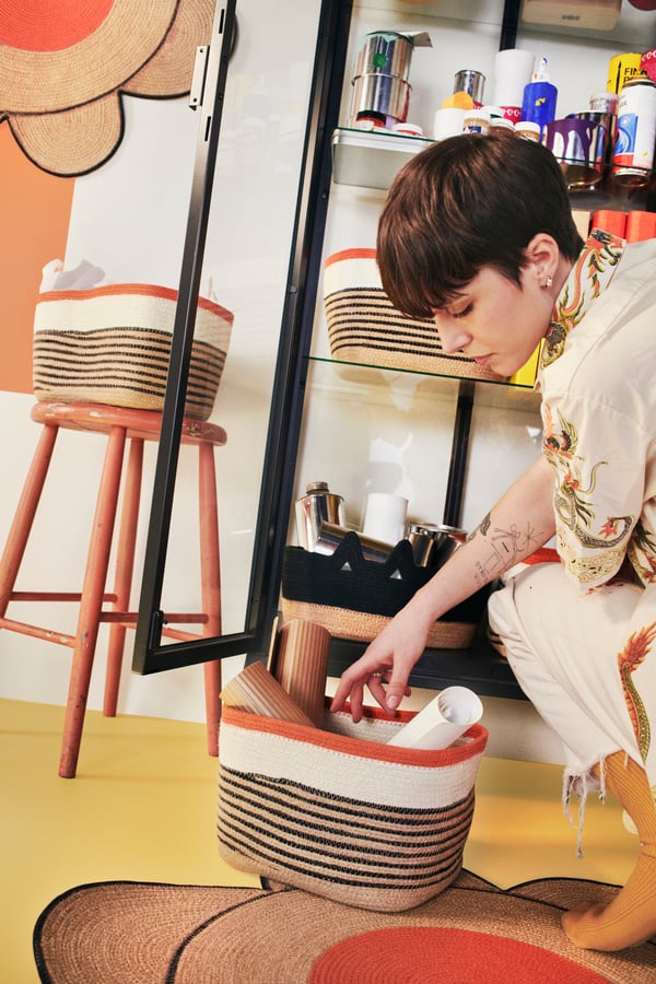 En person står på huk bredvid en tygkorg och letar efter något i korgen. 