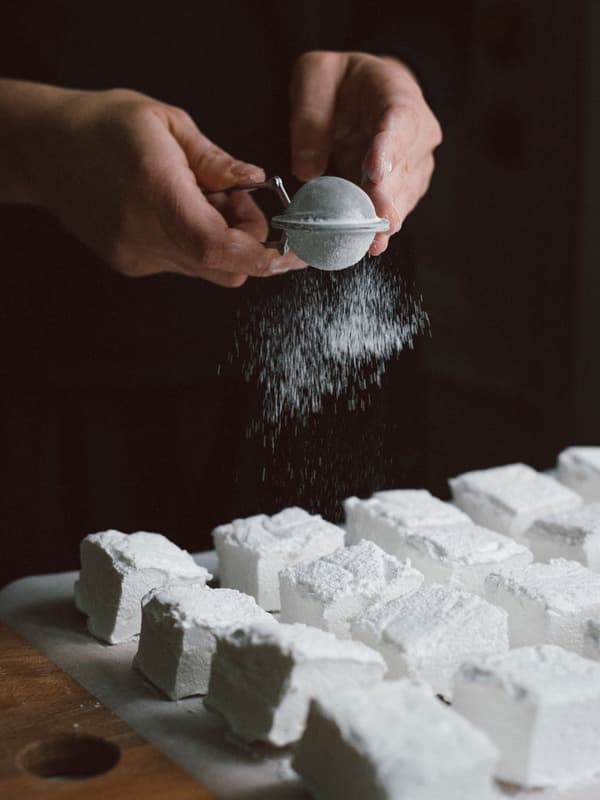 En person strör florsocker på marshmallowsbitar.