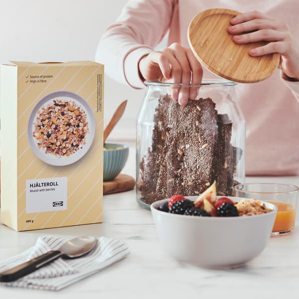 En person tager et stykke brød i en glaskrukke, der står ved siden af en pakke med müsli.