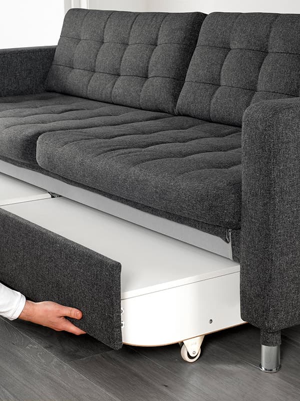 En person trækker sovesofa-funktionen ud på en grå LANDSKRONA sofa.