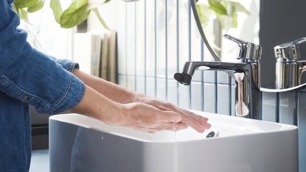 En person tvättar händerna i ett vit handfat.