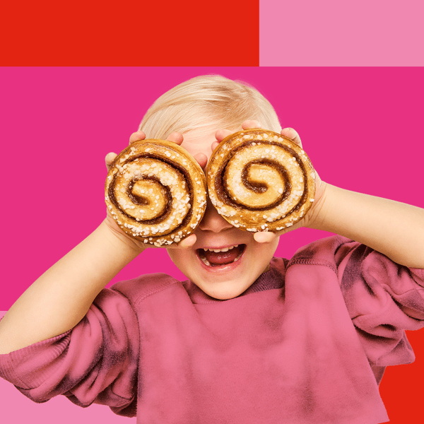 En pige holder to kanelsnegle foran øjnene foran en hvid baggrund.