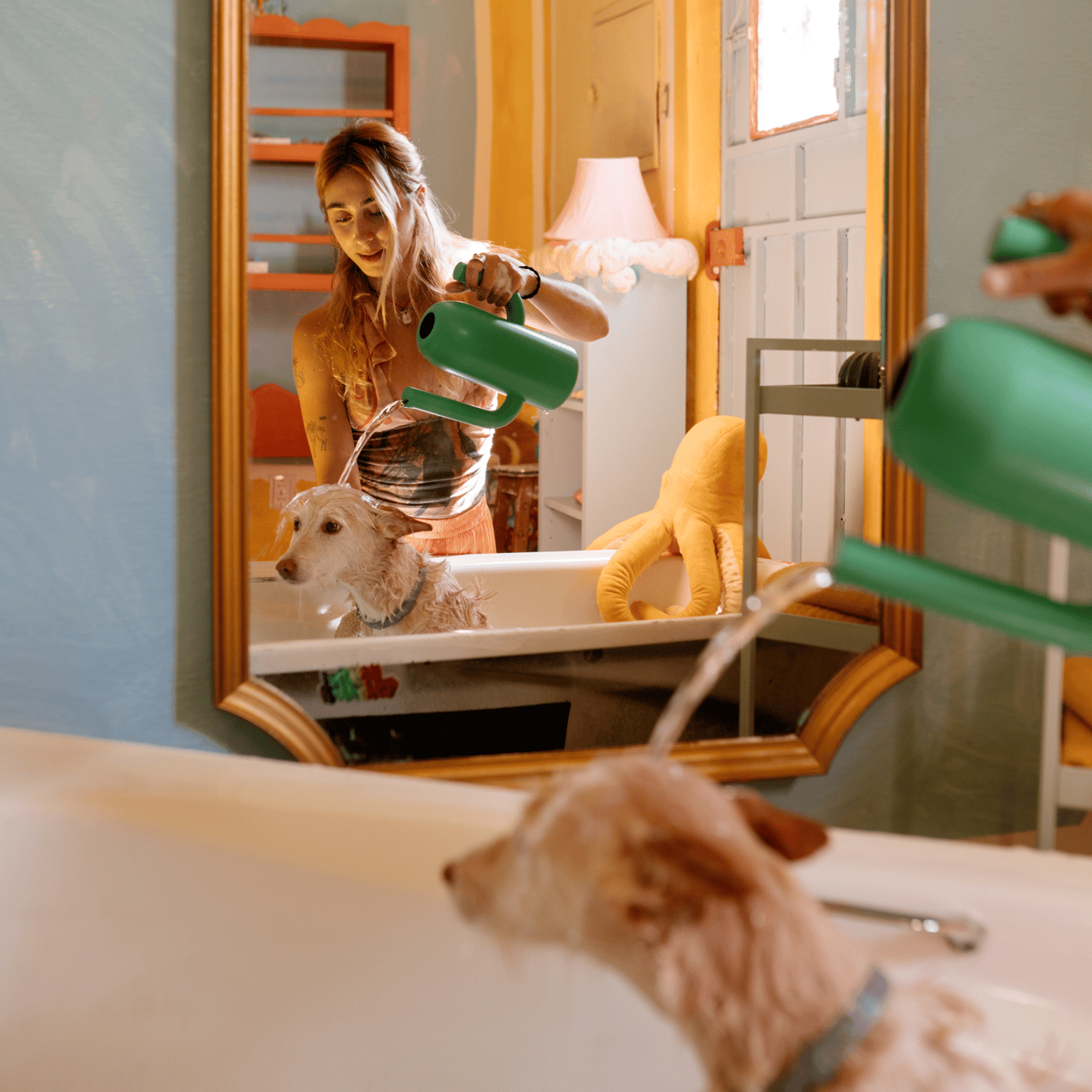 En pige står foran et spejl og vander ned i et badekar på en hund med en grøn ÄRTBUSKE vandkande.
