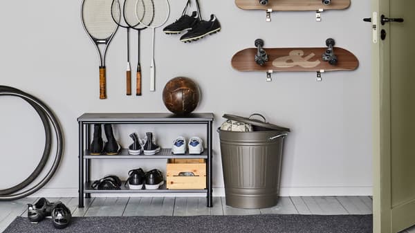 En PINNIG entrébenk med skoplass, med sko og en fotball ved siden av en KNODD dunk med åpent lokk. Racketer og rullebrett henger på veggen bak.