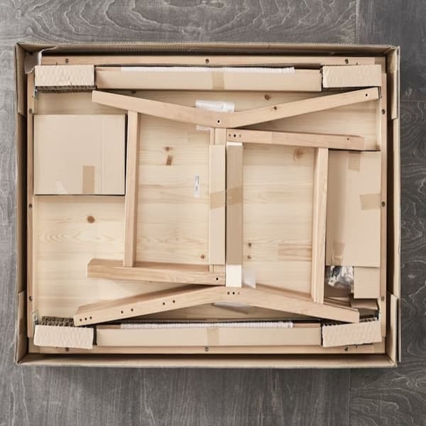 En platt IKEA förpackning med ovansidan borttagen och inuti syns en furustol som väntar på att monteras.