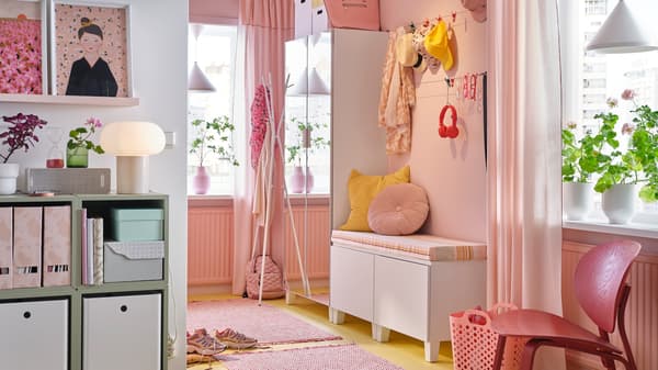 En rosa hall med PLATSA spegelgarderob, bänk med rosa och gula kuddar, en rosa matta och hängande mössor och halsdukar.