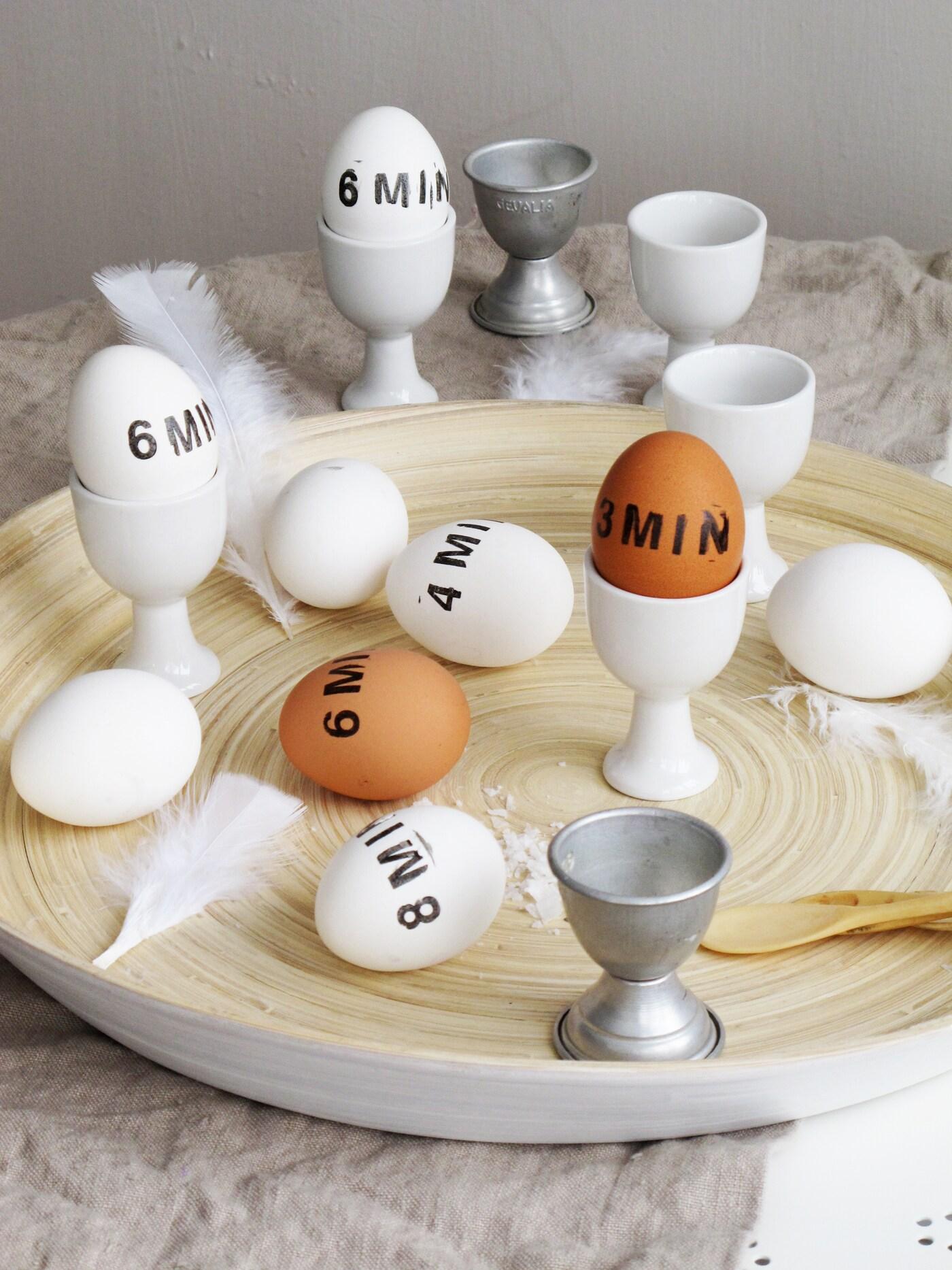 En rund bricka på en naturfärgad duk med massa ägg på. Äggen är stämplade med koktiderna textade, 6 min och 8 minuter på äggen.