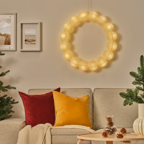 En rundt lampe lyser over en beige sofa med en rød pude og en gul pude. 