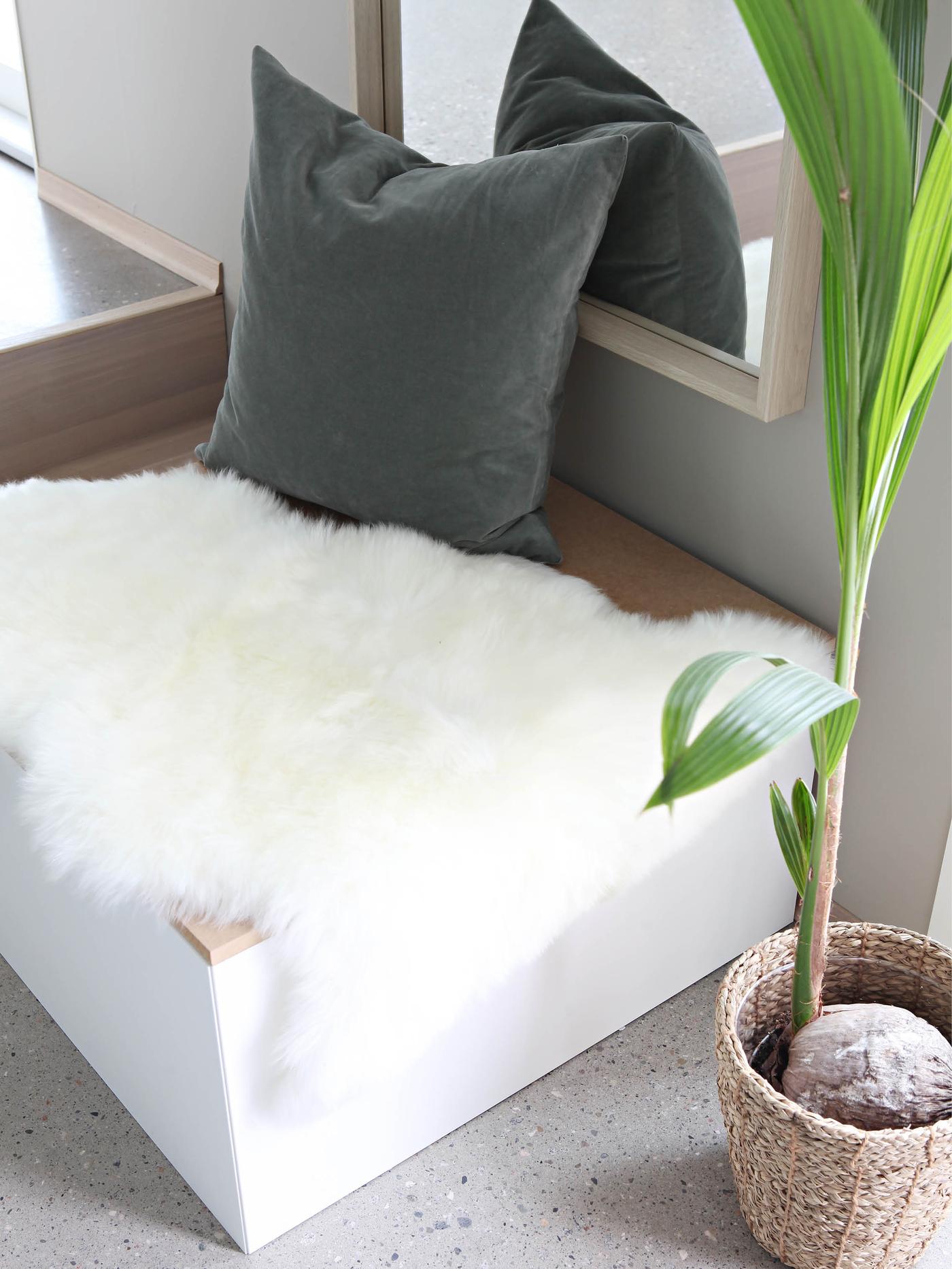 En sittebenk i gangen med saueskinn og en grå pute.