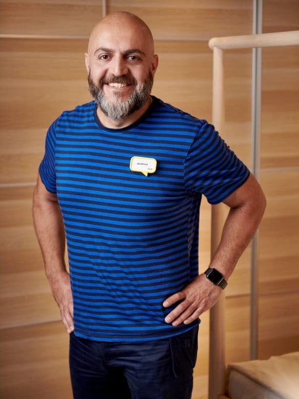 En smiledne Behrooz i en blå IKEA t-shirt foran et skab med skydelåger i træ.