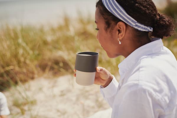 En som sitter drikker kaffe med en reisekrus.