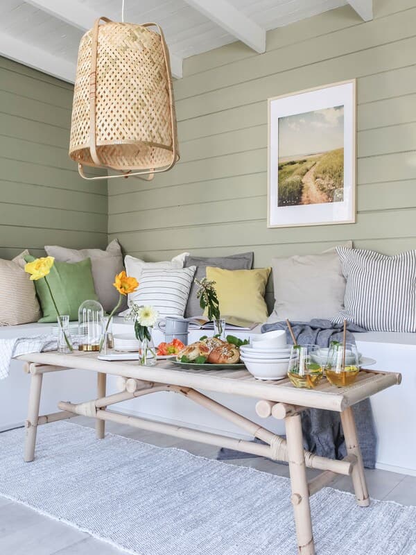 En sommerlig udestue med en hjemmebygget bænk og en masse lyse tekstiler.