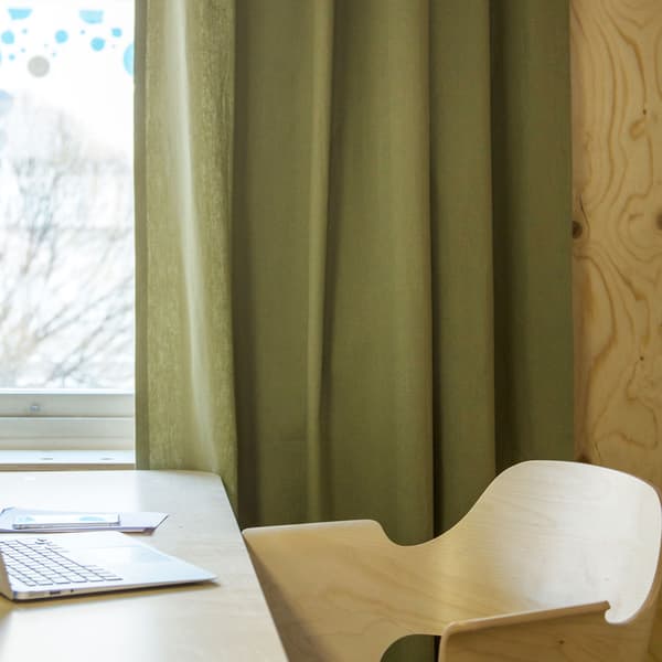 En stol i ljust trä. I badgrunden hänger gröna gardiner med ljus- och ljuddämpande effekt.