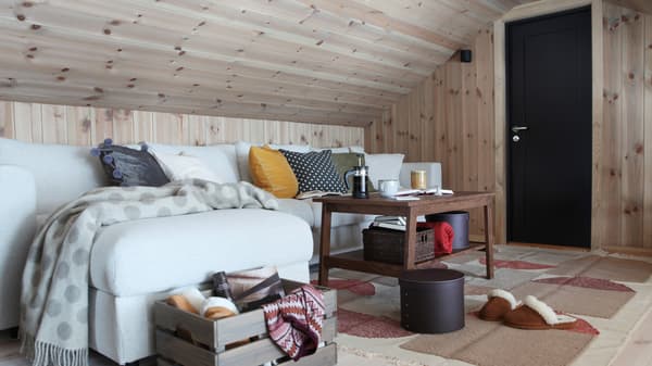 En stue med furu tak og vegger, skråtak, lys sjeselongsofa og brunt stuebord.