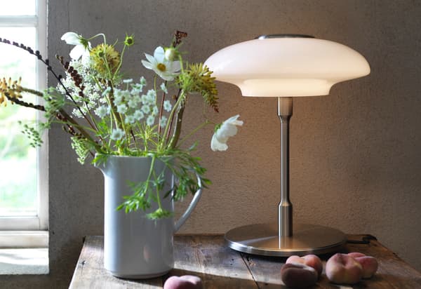 En TÄLLBYN bordlampe ved siden af en buket blomster.