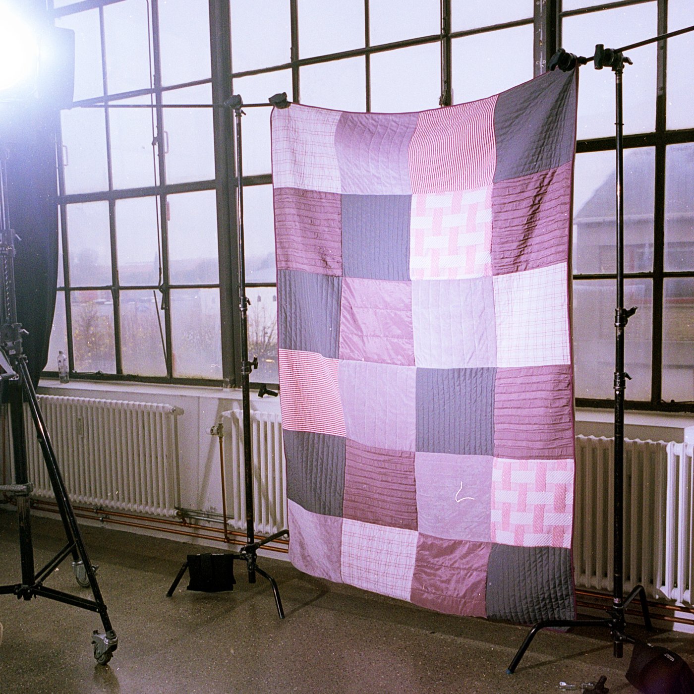 En tæppe der består af mange forskellige farver i firkanter hænger på en snor foran et vindue som en del af FÖRNYA projektet hos IKEA.