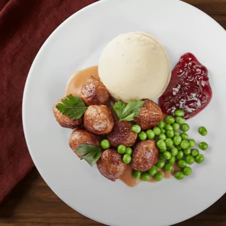 En tallerken med kødboller, kartoffelmos, flødesauce, ærter og tyttebærsyltetøj