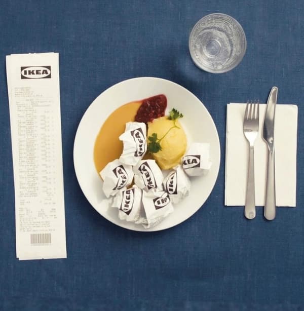 En tallerken med mad og sammenkrøllede IKEA kvitteringer. ses på et blåt bord. Ved siden af tallerkenen ligger en lang IKEA kvittering og bestik på en serviet.