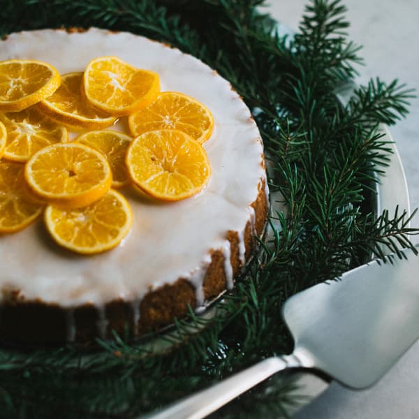 En tårta ligger på ett dekorerat tårtfat och är dekorerat med clementinskivor,