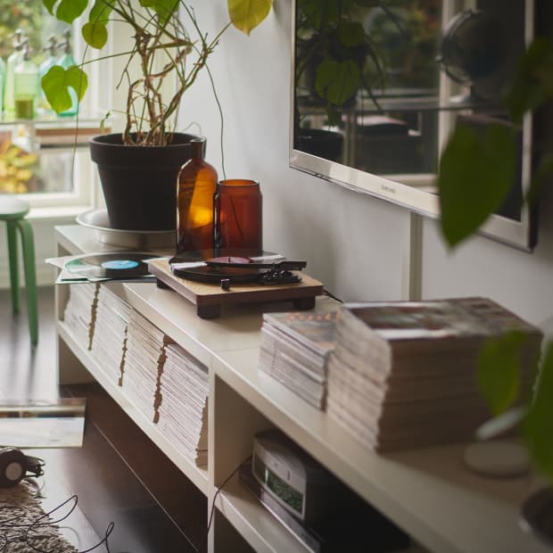 En TV-bänk med dekoration, böcker, vaser och en kruka på. Ovanför hänger en platt-TV på väggen.