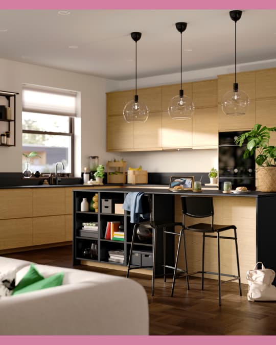 En un apartamento con cocina americana se ve un piso para bar dándole la espalda a la sala.
