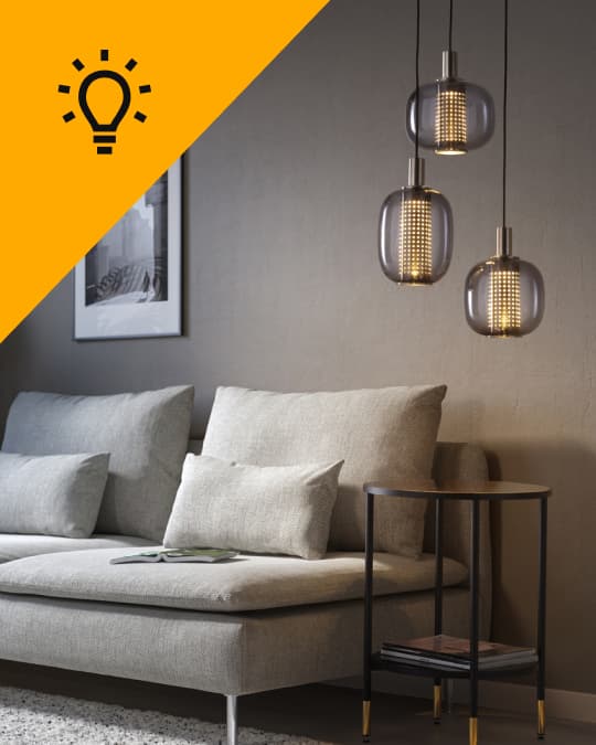 En un living al costado de un sofá hay una lámpara de techo de 3 luminarias que además entrega un diseño moderno al espacio.