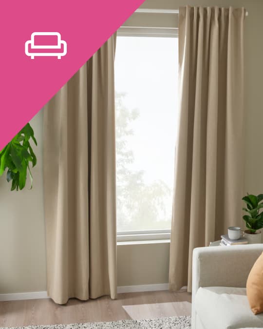 En un living al costado de un sofá unas cortinas de tela beige cubren la mitad de un ventanal.